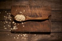 Top view composition with wooden spoon filled with healthy oatmeal flakes placed on cutting board on rustic plank table — Stock Photo