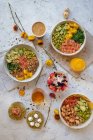 Top view appetizing assorted poke bowls with avocado toasts and glasses of juices served on table with berry dessert near scattered fresh flowers — Stock Photo