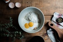 Сверху миска с яйцами и сливками, смешанными с хлебными крошками и мукой на деревянном столе во время приготовления выпечки — стоковое фото