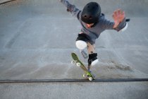 From above of teen boy showing stunt on skateboard while practicing on ramp and jumping in skate park — Stock Photo