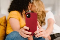 Ernte romantisches lesbisches Paar in lässiger Kleidung küssen einander und machen Selfie auf dem Smartphone, während sie auf dem gemütlichen Sofa sitzen — Stockfoto