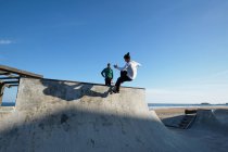 Irreconocible adolescente montar monopatín en skate park en día soleado en la orilla del mar - foto de stock