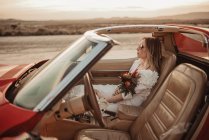 Woman in elegant white dress sitting on passenger seat of luxury vehicle during road trip through Bardenas Reales Natural Park in Navarra, Spain — Stock Photo