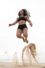 Низкий угол веселой азиатской спортсменки в момент прыжка над песчаным побережьем во время тренировки летом — стоковое фото