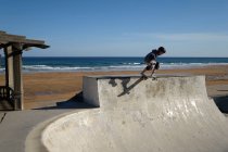 Неузнаваемый подросток в защитном шлеме на скейтборде в скейт-парке в солнечный день на берегу моря — стоковое фото