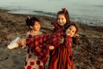Carino piccole ragazze etniche che tengono sorellina sulle mani mentre si divertono insieme sulla spiaggia di sabbia vicino al mare — Foto stock