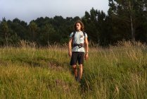 Männlicher Backpacker geht im Sommer bei Sonnenuntergang auf der Wiese spazieren und schaut weg — Stockfoto