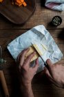 Сверху неузнаваемый человек с помощью ножа режет кусочек масла во время приготовления теста на деревянном столе возле яиц и семян — стоковое фото