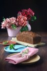 Stillleben eines Biskuitkuchens neben ein paar rosa Vasen mit Blumen auf einem Tisch — Stockfoto