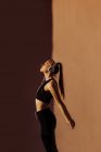Seitenansicht einer jungen athletischen kaukasischen Frau, die Musik hört und sich bei Sonnenuntergang dehnt, Schatten und Licht auf dem Hintergrund — Stockfoto
