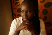 Мирная афроамериканка с плетеной прической, опирающаяся на руки, наслаждаясь выходными в кафе и отводя взгляд — стоковое фото