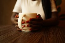 Крупный план анонимной черной женщины с чашкой кофе в кафе — стоковое фото