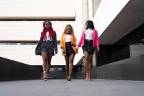 Ground level full body of African American women in stylish wear doing runway walk together near modern building — Stock Photo