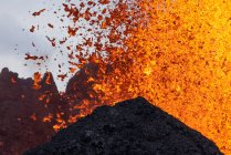 Splashes de lava laranja quente que irrompe do pico da montanha vulcânica cercada de fumaça na Islândia — Fotografia de Stock