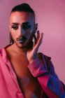 Porträt einer glamourösen Transgender-bärtigen Frau in raffiniertem Make-up, die vor rosa Hintergrund im Studio posiert und wegschaut — Stockfoto