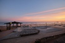 Vista panoramica di skate park situato sulla spiaggia sabbiosa vicino al mare sotto il cielo al tramonto — Foto stock