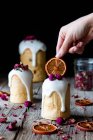 Several delicious homemade kulichs poured with sweet glaze and decorated with pieces of dry orange and flowers on wooden table — Stock Photo