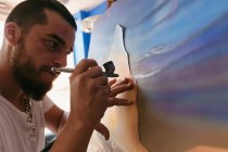 Side view of male artist using spray gun to paint picture on canvas during work in creative workshop — Stock Photo