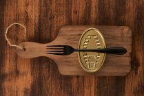Dall'alto tagliere graffiato con forchetta e lattina sigillata con cibo conservato sul tavolo in legno rustico — Foto stock