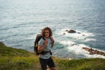 Mochilero masculino caminando en la colina durante el trekking en verano y mirando hacia otro lado - foto de stock