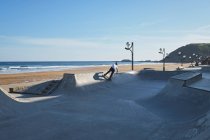 Irreconhecível teen menino equitação skate no skate parque no ensolarado dia no litoral — Fotografia de Stock