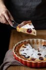 Pessoa sem rosto em pé à mesa com pedaço cortado de torta saborosa com cerejas — Fotografia de Stock