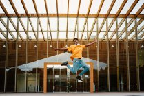 Низький кут повний тіла афроамериканського чоловіка з навушниками на шиї стрибає високо з витягнутими руками — стокове фото
