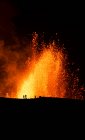 Silhouette di viaggiatori anonimi in piedi contro il fumo arancione del vulcano attivo in Islanda — Foto stock