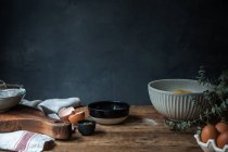 Чаша с яйцами, мукой и деревянной ложкой с тыквенным пюре на деревянном столе во время приготовления выпечки на тёмном фоне — стоковое фото