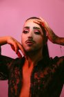 Портрет гламурной трансгендерной бородатой женщины в сложном макияже, позирующей перед камерой на розовом фоне в студии — стоковое фото