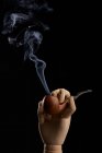 Традиционная табачная трубка с дымом в деревянной руке на черном фоне в студии — стоковое фото