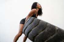 Niedrige Seitenansicht muskulöser asiatischer Athletin, die während des intensiven Trainings schwere Reifen umkippt — Stockfoto