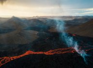 Drone vista del arroyo de lava naranja caliente que fluye a través del terreno montañoso en la mañana en Islandia - foto de stock