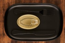 Top view of black fork and knife placed near sealed canned food on rectangular black tray — Stock Photo