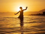 Silhouette of anonymous little man standing in sea water against sunset light in summertime — Stock Photo