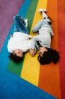 Von oben fröhliche junge homosexuelle Freundinnen, die eng am regenbogenfarbenen Boden liegen und Spaß haben — Stockfoto