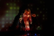 Счастливая девушка ди-джей в наушниках улыбается и использует синтезатор для воспроизведения музыки, стоя в дыму во время вечеринки в ночном клубе — стоковое фото