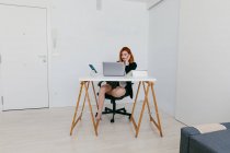 Jungunternehmerin arbeitet zu Hause am Netbook am Schreibtisch mit Tablet und Smartphone — Stockfoto