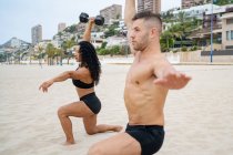 Seitenansicht muskulöser multiethnischer Sportler, die im Sommer am Sandstrand mit Kurzhanteln trainieren — Stockfoto