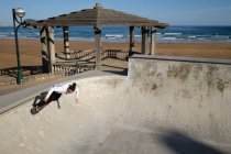 Неузнаваемый юноша катается на скейтборде в скейт-парке в солнечный день на берегу моря — стоковое фото