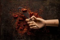 Top view composition with spilled aromatic natural ground sun dried tomatoes on dark table with knife in artificial wooden hand — Stock Photo
