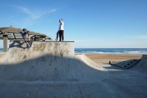 Pattinatori attivi cavalcando skateboard e mostrando trucchi in skate park al mare in estate — Foto stock