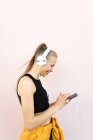 Giovane donna caucasica che indossa cuffie e abbigliamento sportivo, ascolta musica al telefono e sorride, isolata su uno sfondo luminoso — Foto stock