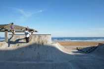 Patinadores ativos andando de skate e mostrando truques no parque de skate à beira-mar no verão — Fotografia de Stock
