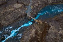 Vista desde arriba del dron del puente que cruza el arroyo rápido con agua azul en terreno accidentado en Islandia - foto de stock