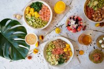Top view appetizing assorted poke bowls with avocado toasts and glasses of juices served on table with berry dessert near scattered fresh flowers — Stock Photo
