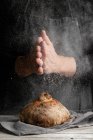 Unrecognizable chef in apron standing at table and decorating loaf of traditional bread with flour — Stock Photo