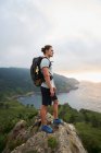 Вид збоку чоловічий мандрівник стоїть на скелі і захоплюючий вид на море під час походу влітку — стокове фото