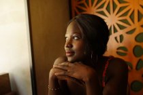 Мирная афроамериканка с плетеной прической, опирающаяся на руки, наслаждаясь выходными в кафе и отводя взгляд — стоковое фото