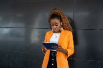 African American female in elegant stylish wear surfing tablet while standing in corridor — Stock Photo